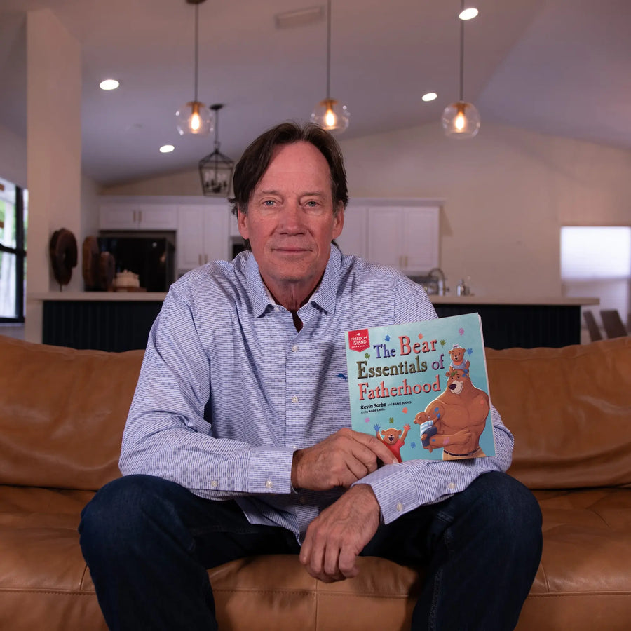 Kevin Sorbo sitting holding his children's book, The Bear Essentials of Fatherhood