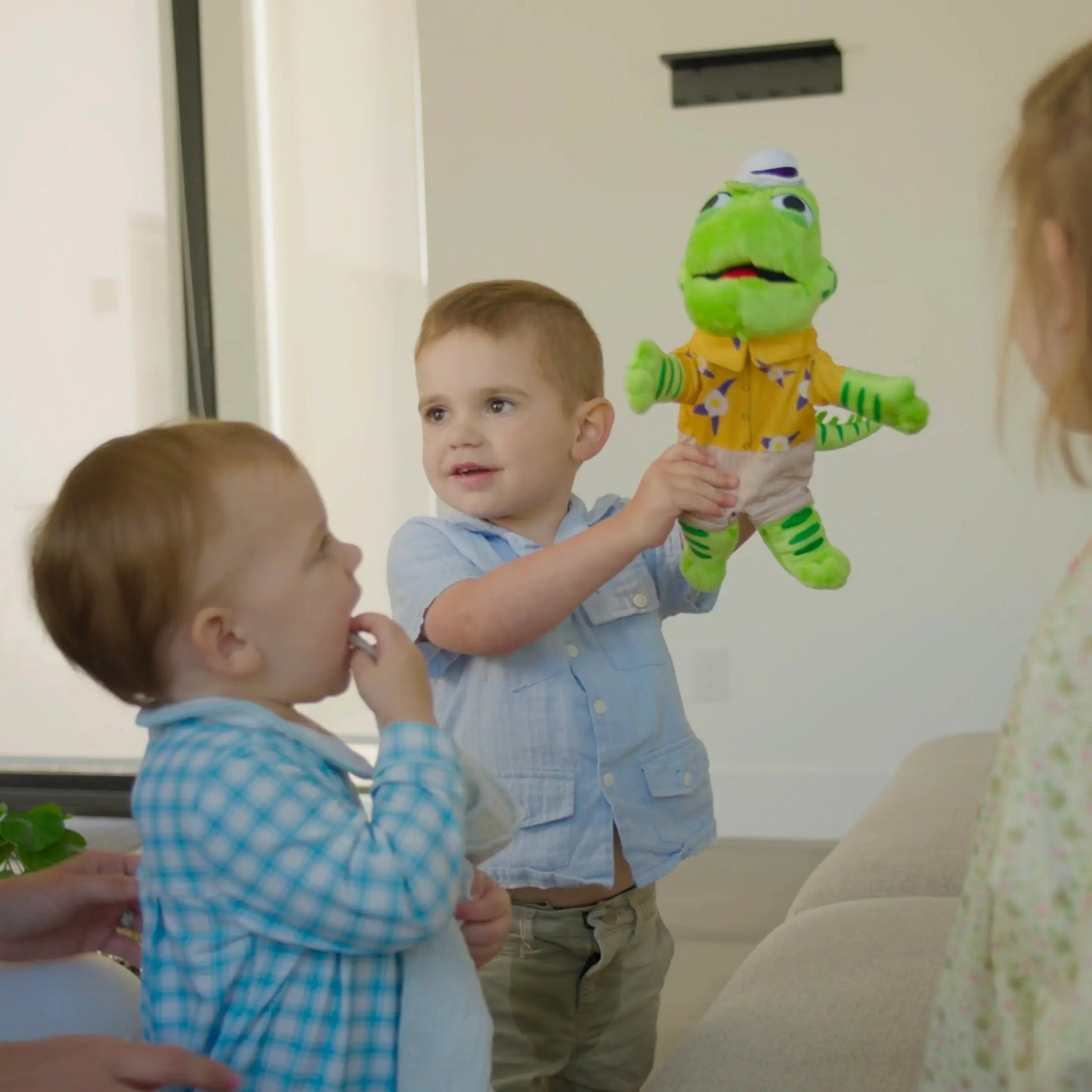 Two children playing with an iguana puppet toy in a room with a woman and another child.