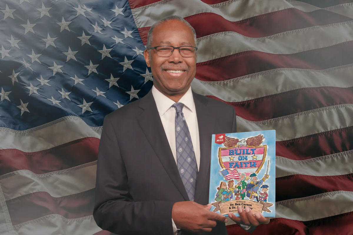Dr. Ben Carson holding a book titled 'Built on Faith' against an American Flag background