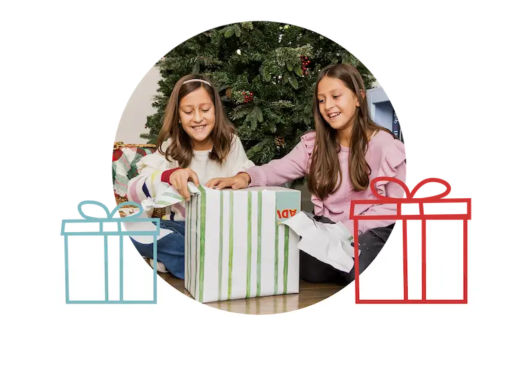 2 little girls unwrapping a gift next to a Christmas tree