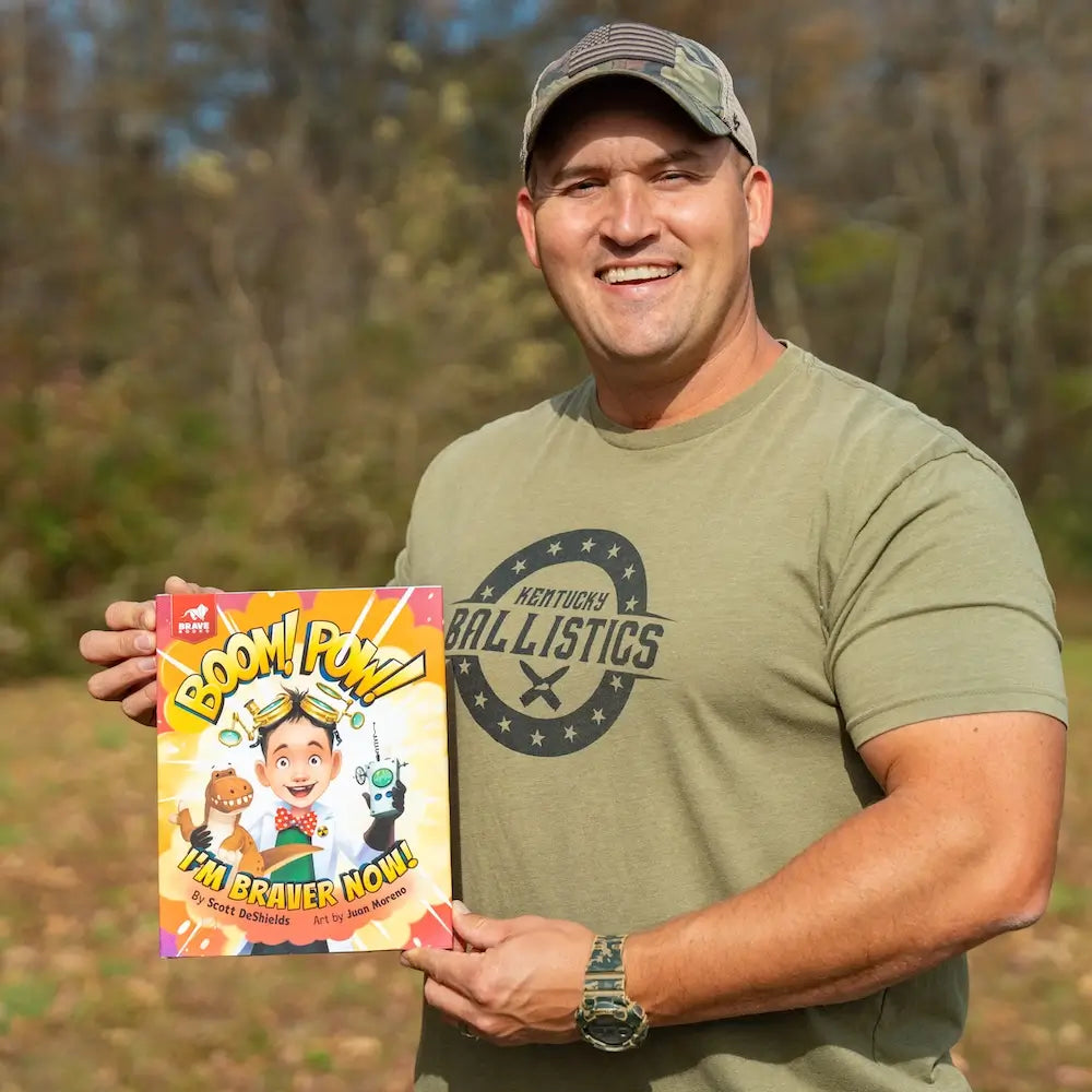 Kentucky Ballistics is holding a book titled 'BOOM! POW! I'm Braver Now!' outdoors
