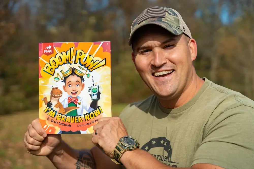 Kentucky Ballistics holding a book titled 'Boom! Pow! I'm Braver Now!' outdoors