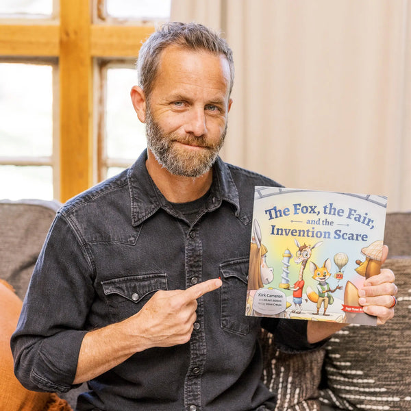 Man holding a book titled 'The Fox, the Fair, and the Invention Scare' in a home setting.