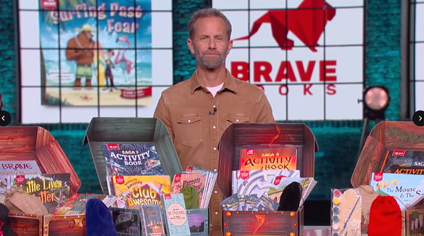 Kirk Cameron standing behind a display of children's books and activity sets with 'Brave Books' branding in the background.