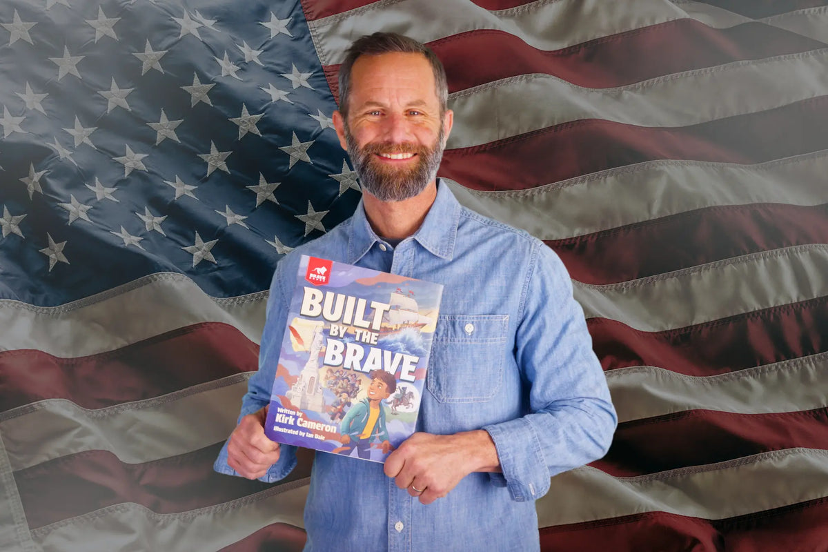 Kirk Cameron holding a book titled 'Built for the Brave' in front of an American flag