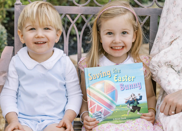 Two children holding a book titled 'Saving the Easter Bunny' outdoors.