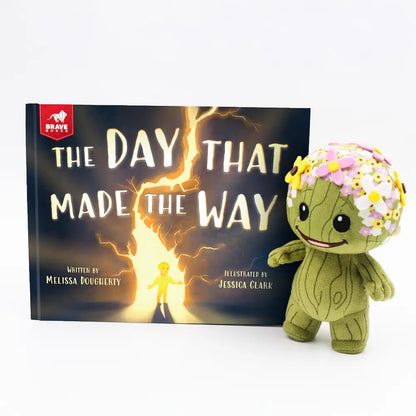 Book titled 'The Day That Made The Way' by Melissa Dougherty with a green plush toy in front on a white background